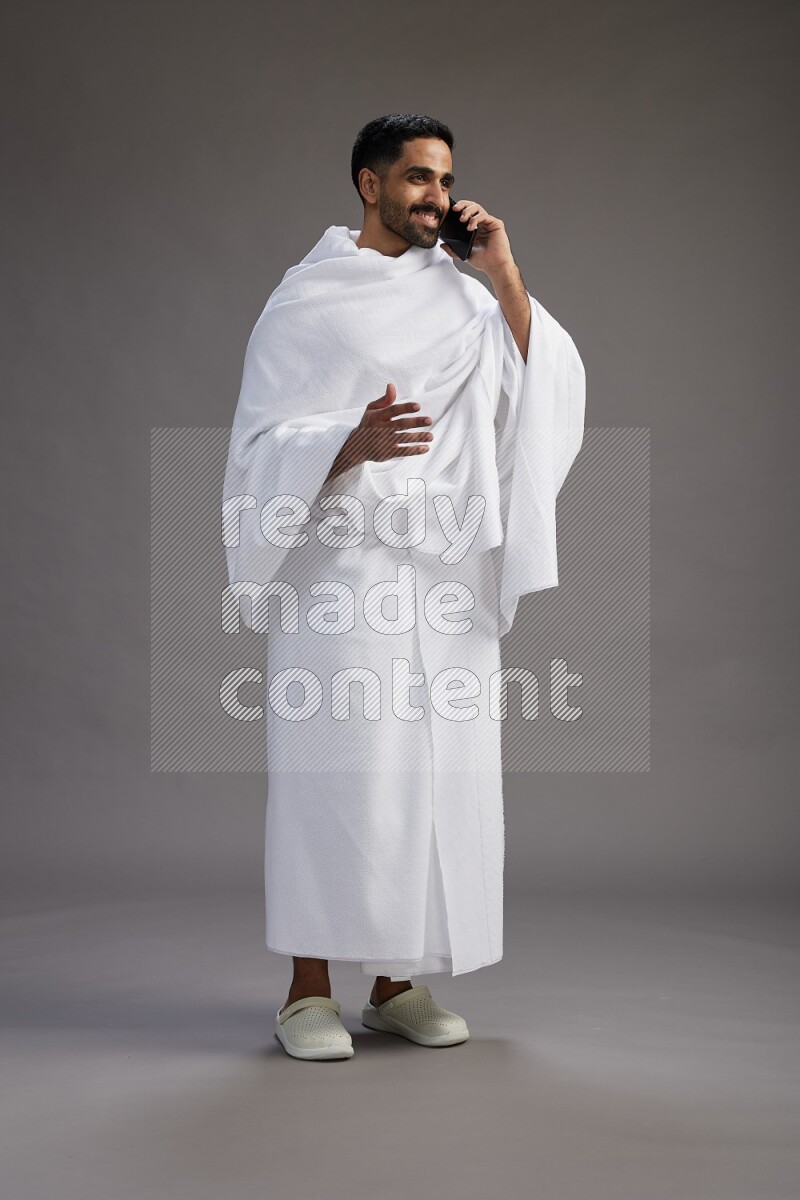 A man wearing Ehram Standing talking on phone on gray background