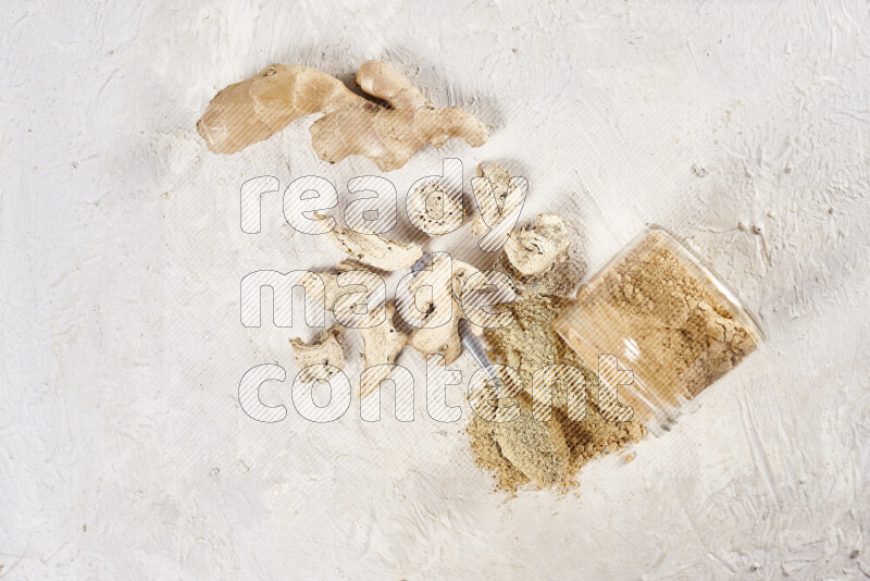 A glass jar full of ground ginger powder flipped with some spilling powder on white background