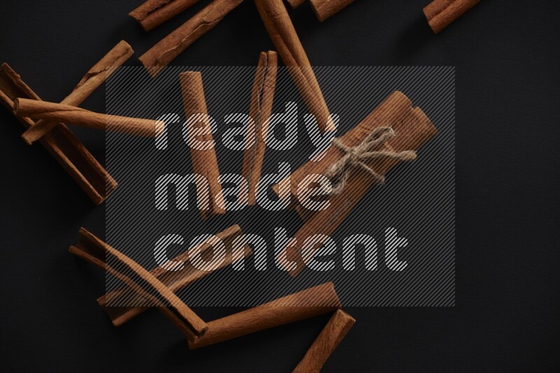 4 Cinnamon sticks stacked and bounded with more sticks in the background on black flooring