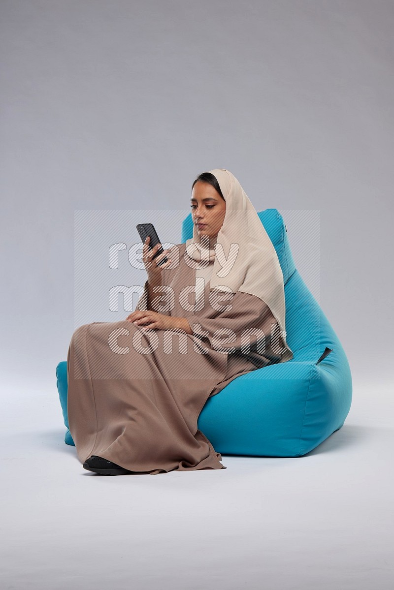 A Saudi woman sitting on a blue beanbag and texting on phone