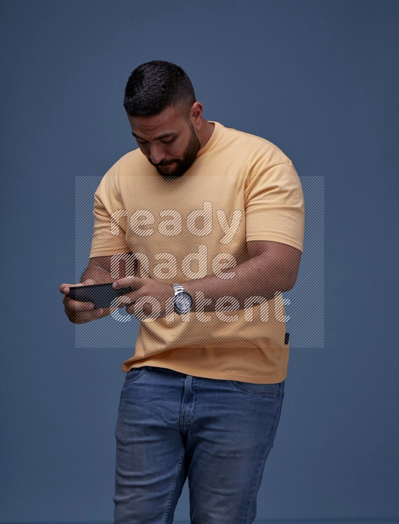 رجل يرتدي بنطال ازرق جينز وقميص اصفر بأكمام قصيره يلعب في جواله