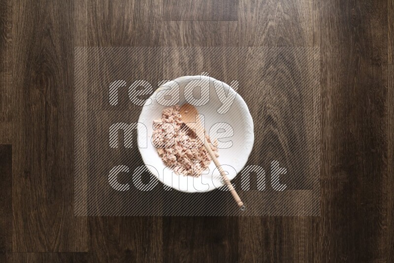 A white bowl full of tuna, colored bell pepper, sour cream, corn, parsley, black pepper powder and sauce, with wooden spoon on wooden background