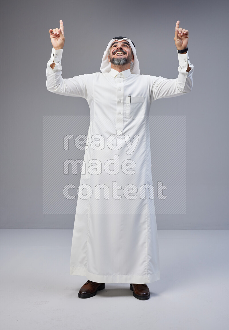 Saudi man Wearing Thob and white Shomag standing interacting with the camera on Gray background