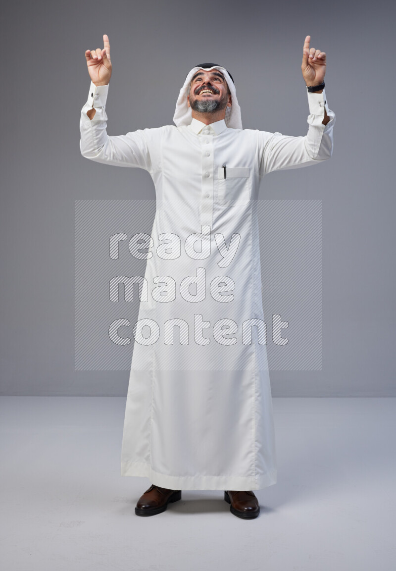 Saudi man Wearing Thob and white Shomag standing interacting with the camera on Gray background