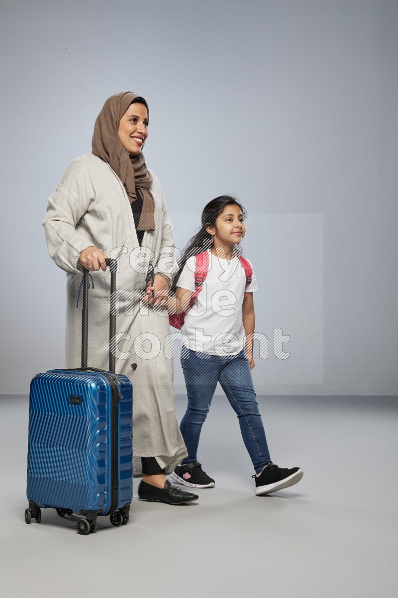 Mom and daughter standing pulling a carry-on bag on gray background