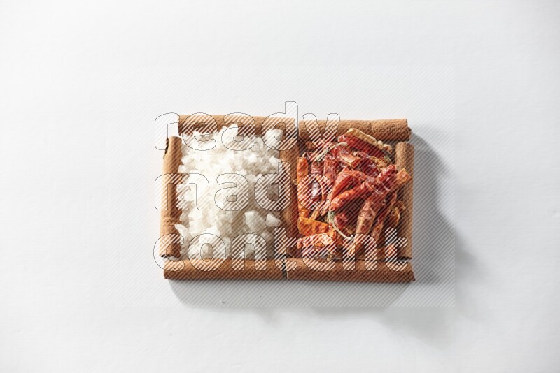 مربعان من أعواد القرفة ممتلئان بالفلفل الحار المجفف والملح الأبيض علي خلفية بيضاء