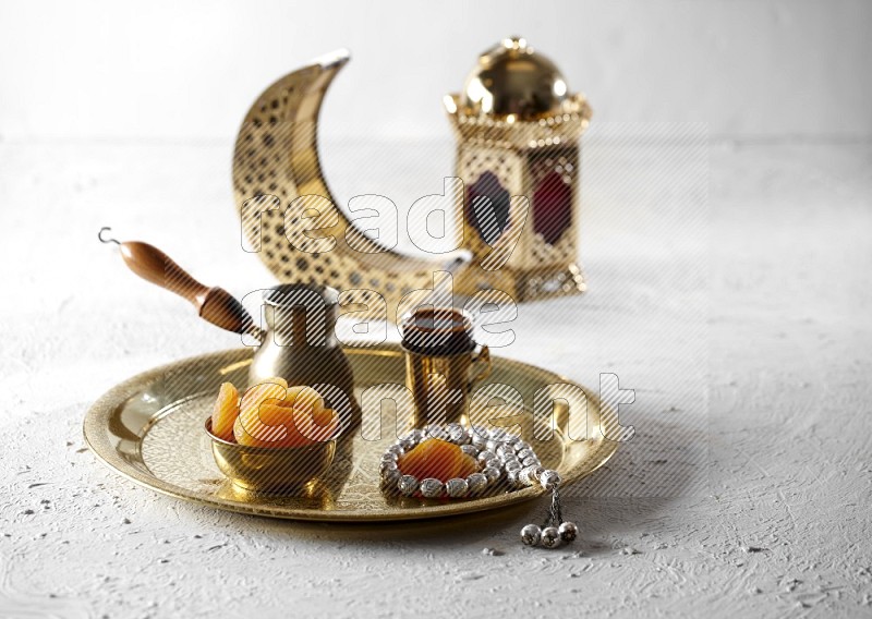 Dried apricots in a metal bowl with coffee and prayer beads on a tray beside lanterns in a light setup