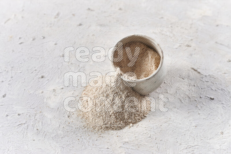 A beige pottery bowl full of onion powder with fallen powder from it on white background