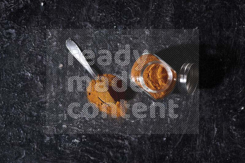 A glass jar full of ground paprika powder on black background