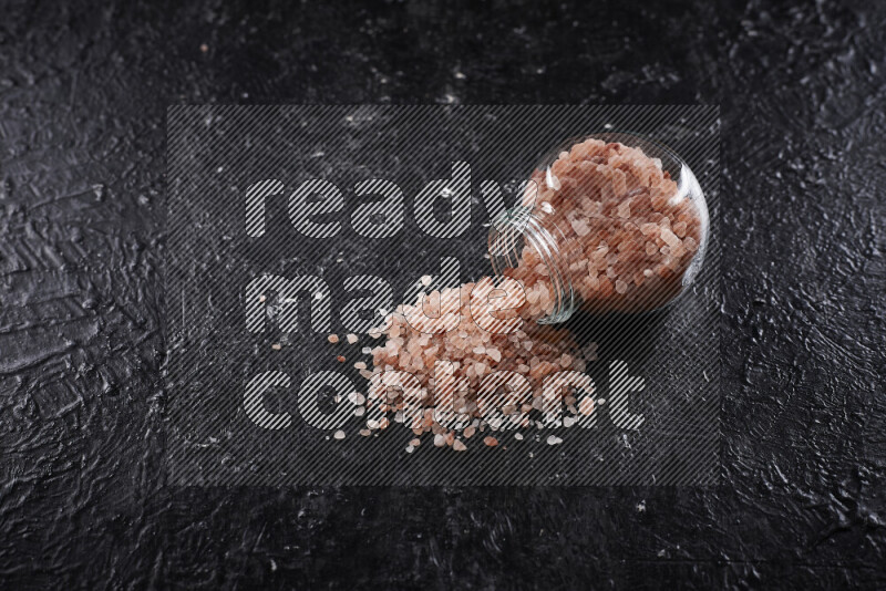 A glass jar full of coarse himalayan salt crystals on black background