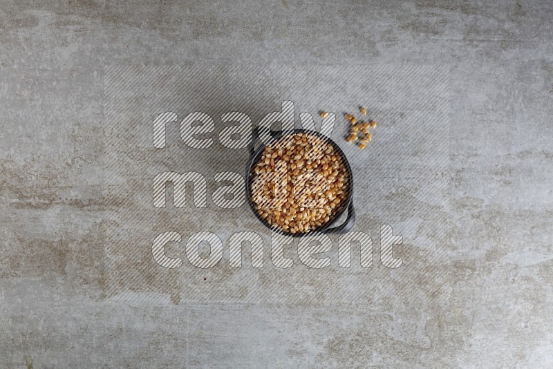 corn kernel in a black handheld ceramic bowl on a grey textured countertop
