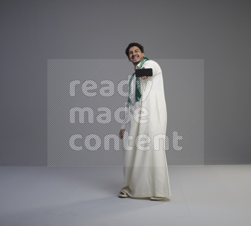 رجل سعودي يرتدي ثوب ابيض و شال يحمل جوال