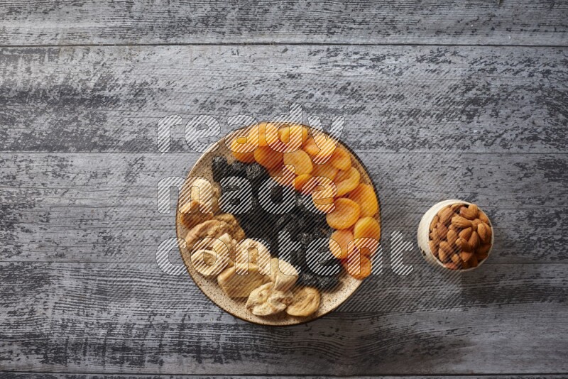 Dried fruits in a pottery plate with nuts and coffee in a dark setup