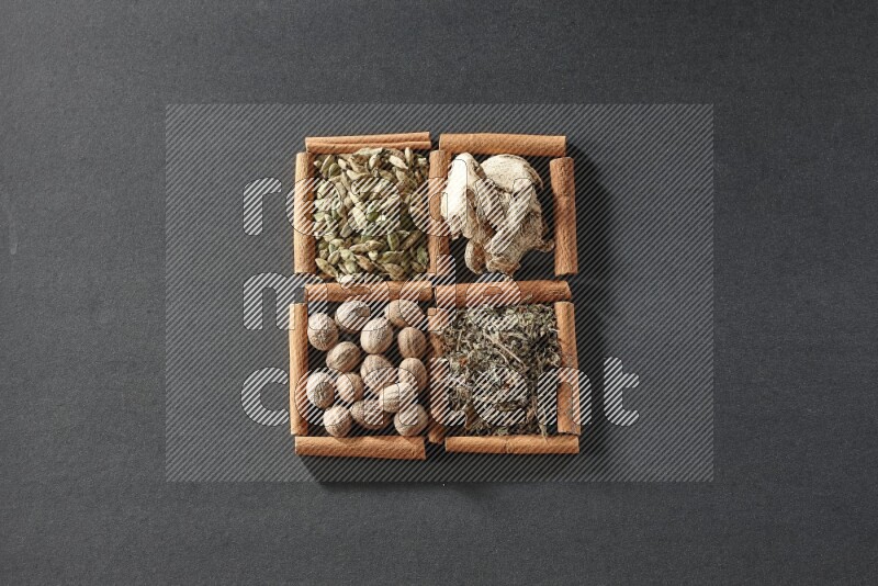 4 مربعات من عيدان القرفة ممتلئة بالريحان المجفف والهيل والزنجبيل المجفف وجوزة الطيب على أرضية سوداء