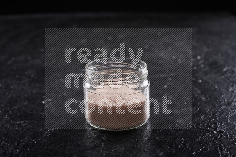 A glass jar full of fine himalayan salt on black background