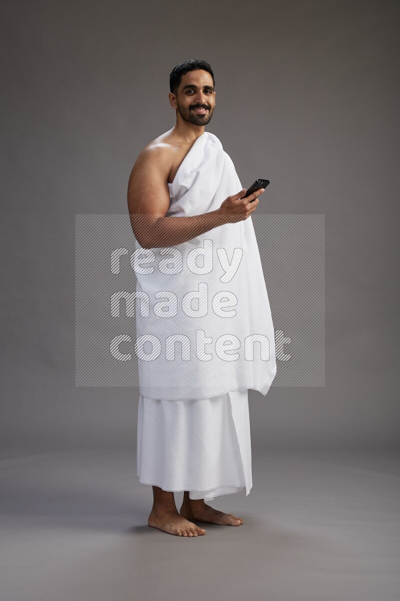 A man wearing Ehram Standing texting on phone on gray background