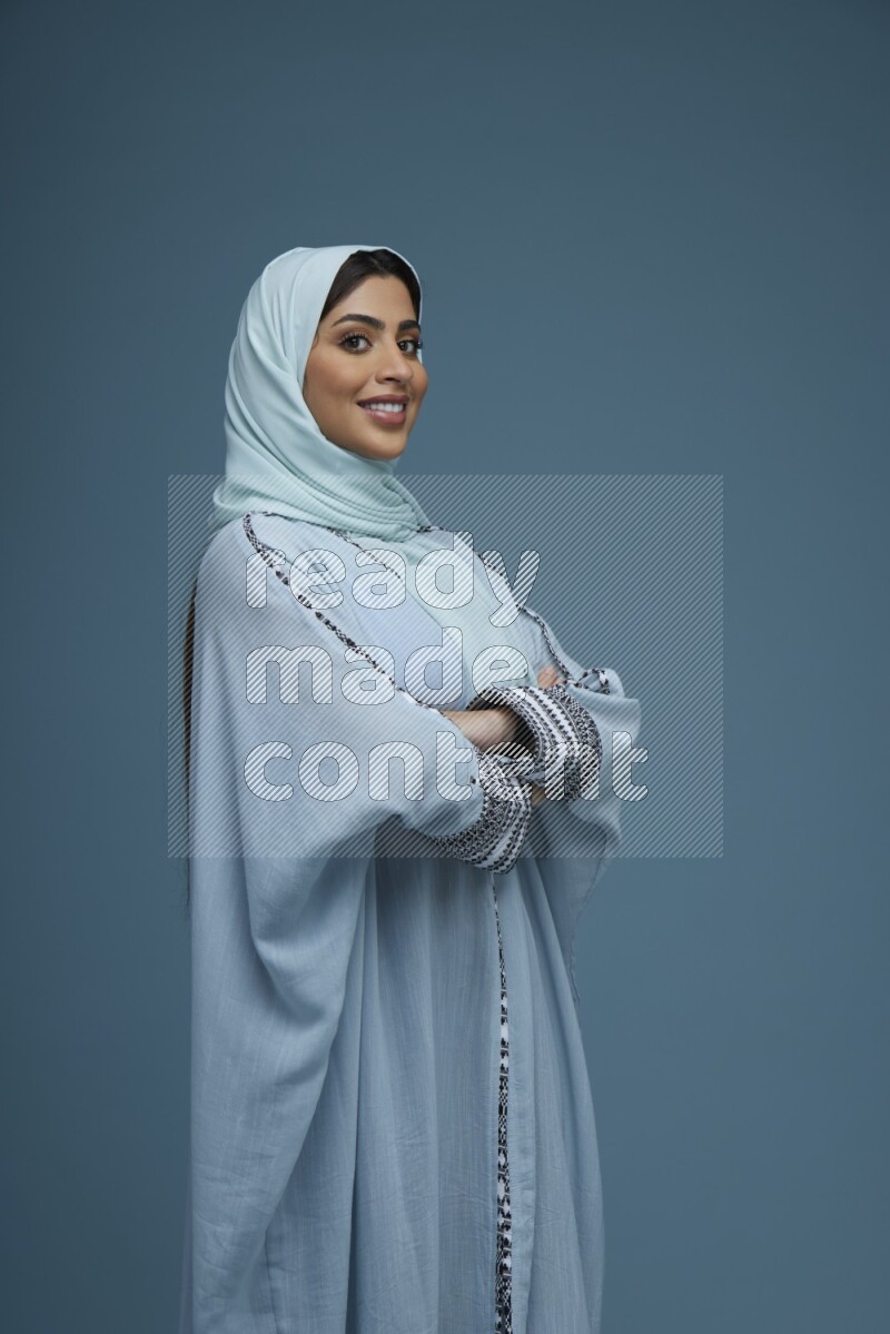 A woman posing in a blue background wearing a blue Abaya with hijab