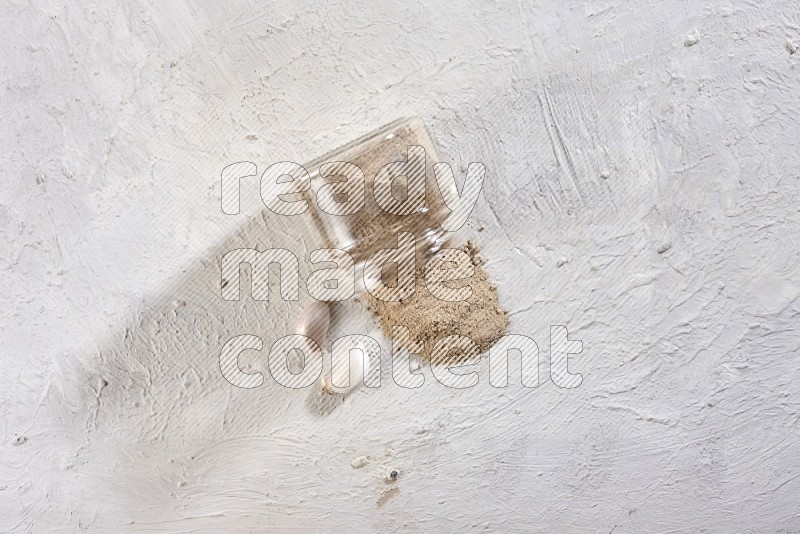 A glass jar full of garlic powder flipped over with the powder came out on a textured white flooring