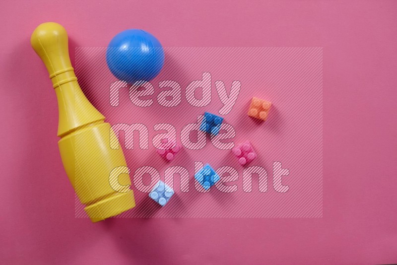 Plastic building blocks, balls and bowling pins on pink background in top view (kids toys)