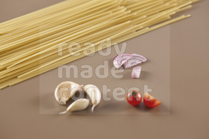 Raw pasta with different ingredients such as cherry tomatoes, garlic, onions, red chilis, black pepper, white pepper, bay laurel leaves, rosemary and cardamom on beige background