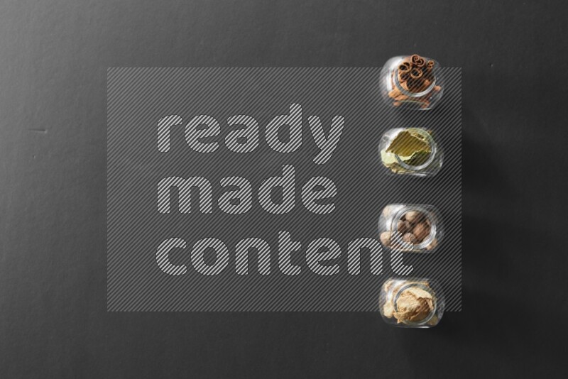 أوراق الغار وزنجبيل مجفف وقرفة وجوزة الطيب في أوعية زجاجية علي خلفية سوداء