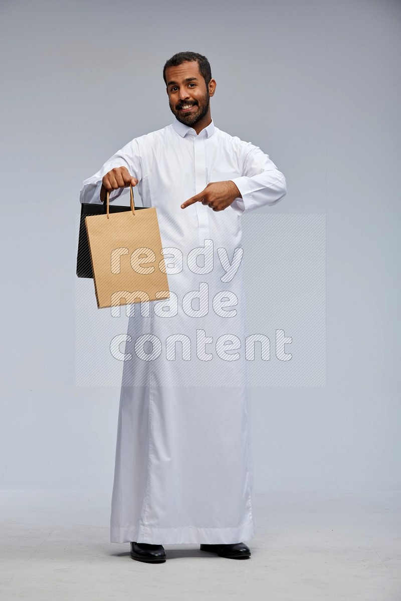 Saudi man Wearing thob standing holding shopping bag on Gray background