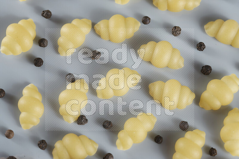 Raw pasta with different ingredients such as cherry tomatoes, garlic, onions, red chilis, black pepper, white pepper, bay laurel leaves, rosemary, cardamom and mushrooms on light blue background