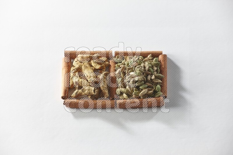 مربعان من أعواد القرفة ممتلئان بحبوب الهيل وأصابع الكركم علي خلفية بيضاء