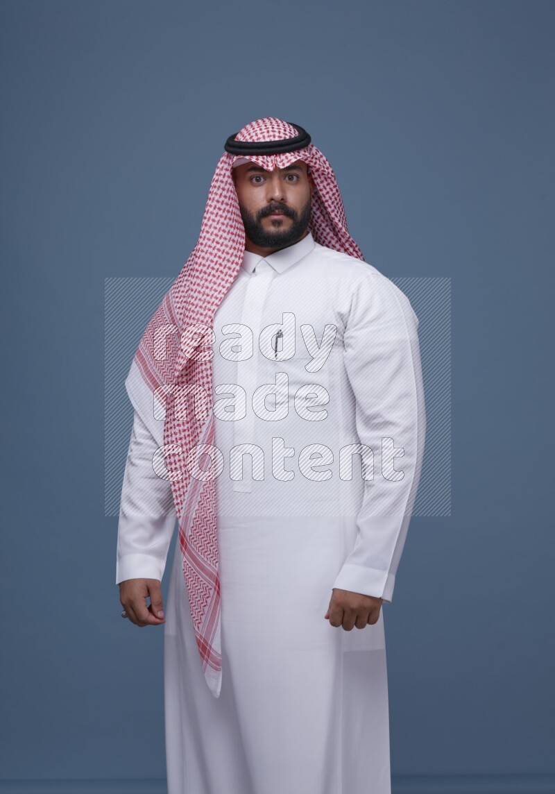 A Saudi man posing on blue background wearing Thob and Shomag