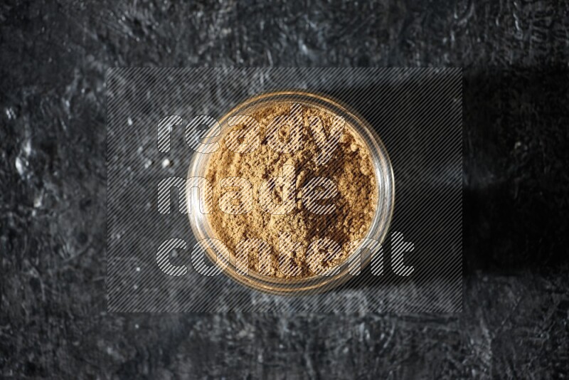 A glass jar full of allspice powder on a textured black flooring