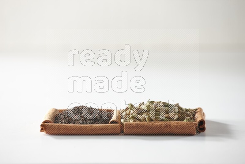 مربعان من أعواد القرفة ممتلئان بحبوب الهيل والشاي الأسود علي خلفية بيضاء