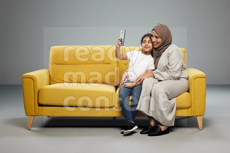 A girl sitting taking selfie with her mother on gray background