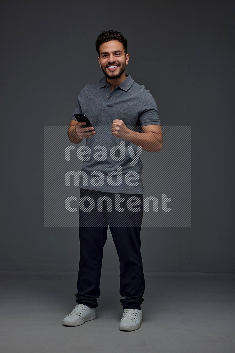 A man wearing casual standing and using his phone eye level on a gray background