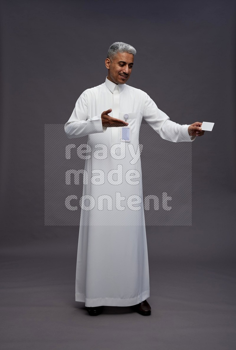 Saudi man wearing thob with pocket employee badge standing holding ATM card on gray background