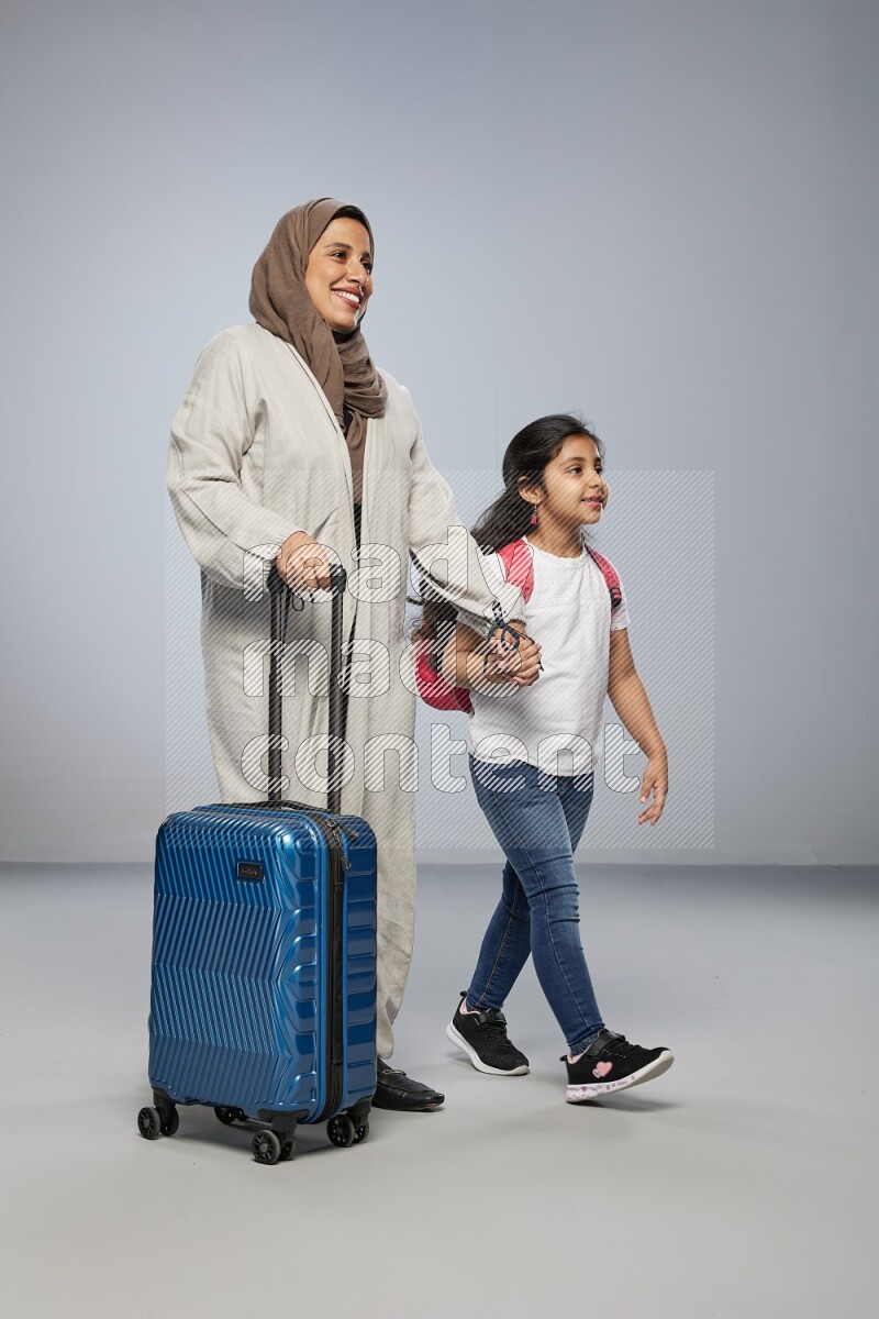 Mom and daughter standing pulling a carry-on bag on gray background