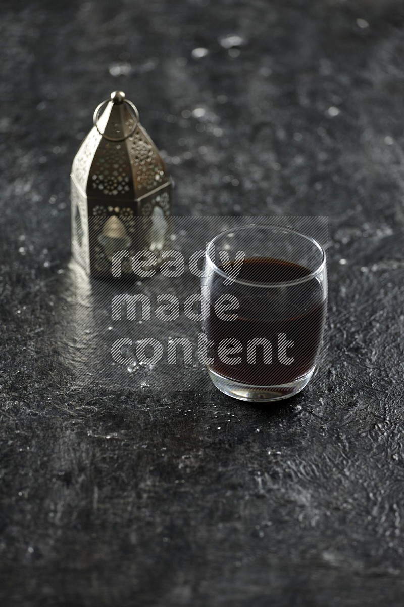 A silver lantern with different drinks, dates, nuts, prayer beads and quran on textured black background