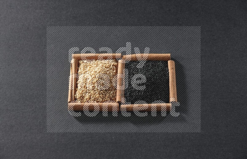 مربعان من أعواد القرفة ممتلئان ببذور السمسم وحبة البركة السوداء علي خلفية سوداء