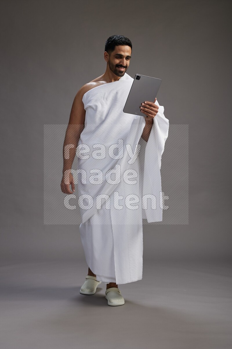 A man wearing Ehram and holding a tablet on gray background