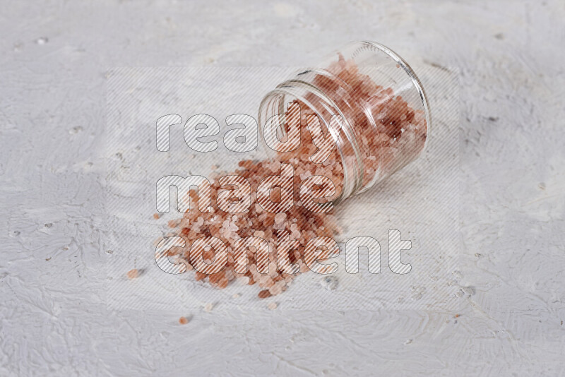 A glass jar full of coarse himalayan salt crystals on white background