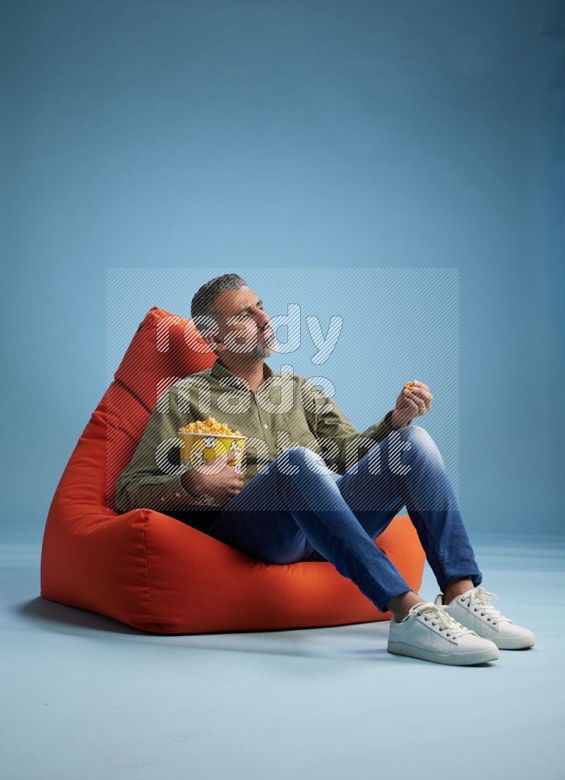 A man sitting on an orange beanbag and eating popcorn