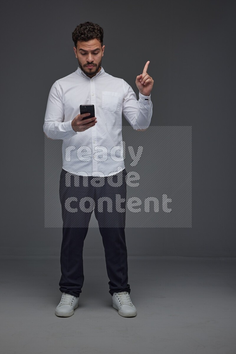 A man wearing smart casual standing and using his phone and making multi hand gestures eye level on a gray background