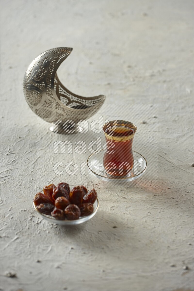 A silver lantern with different drinks, dates, nuts, prayer beads and quran on textured white background