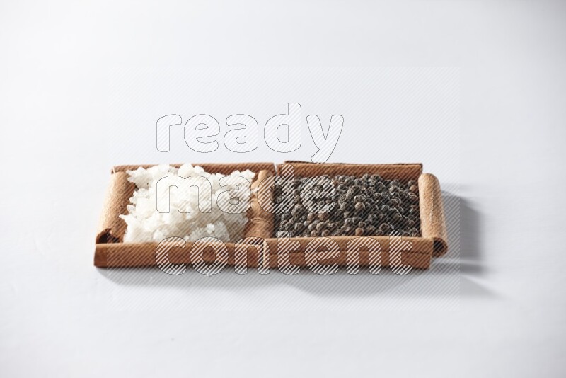 2 squares of cinnamon sticks full of black pepper and white salt on white flooring