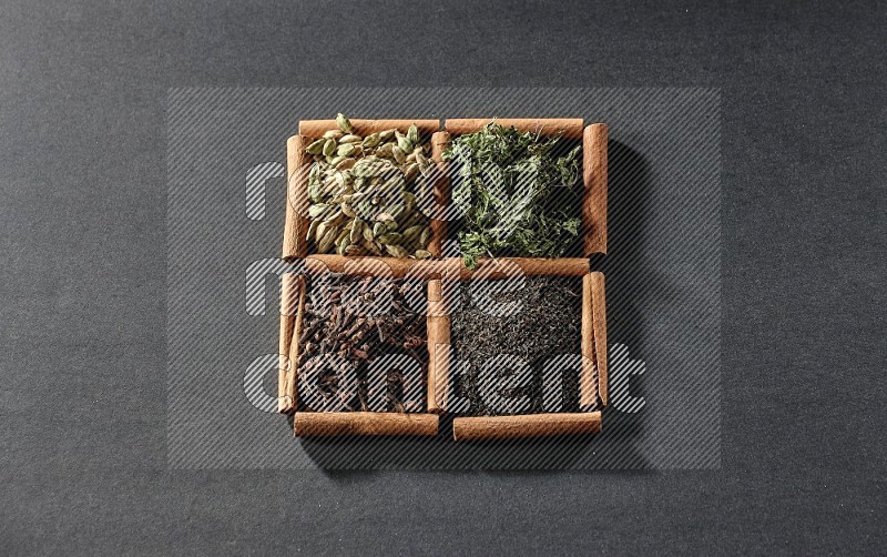 4 squares of cinnamon sticks full of black tea, cloves, dried mint leaves and cardamom on black flooring