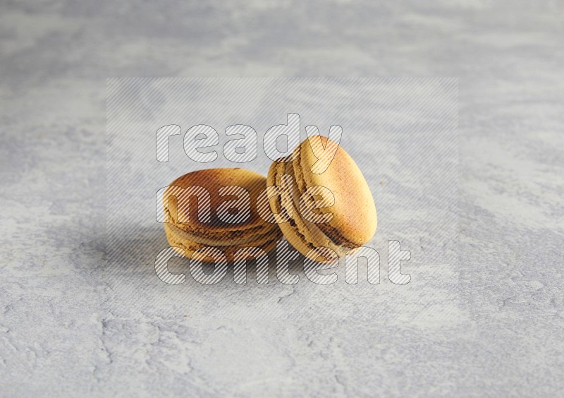 45º Shot of two Yellow Crème Brulée macarons on white  marble background