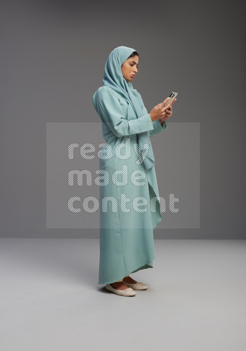 Saudi Woman wearing Abaya standing texting on phone on Gray background