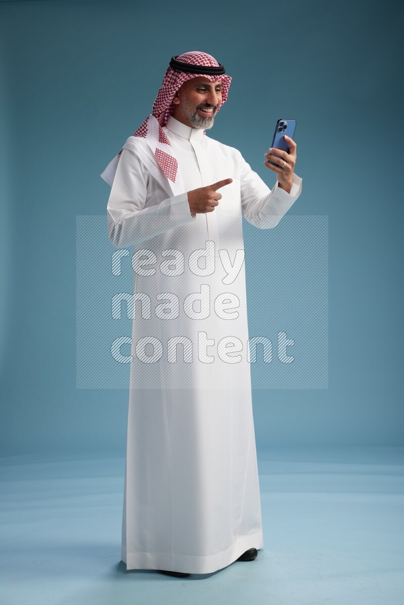 Saudi man wearing thob and shomagh texting on blue background