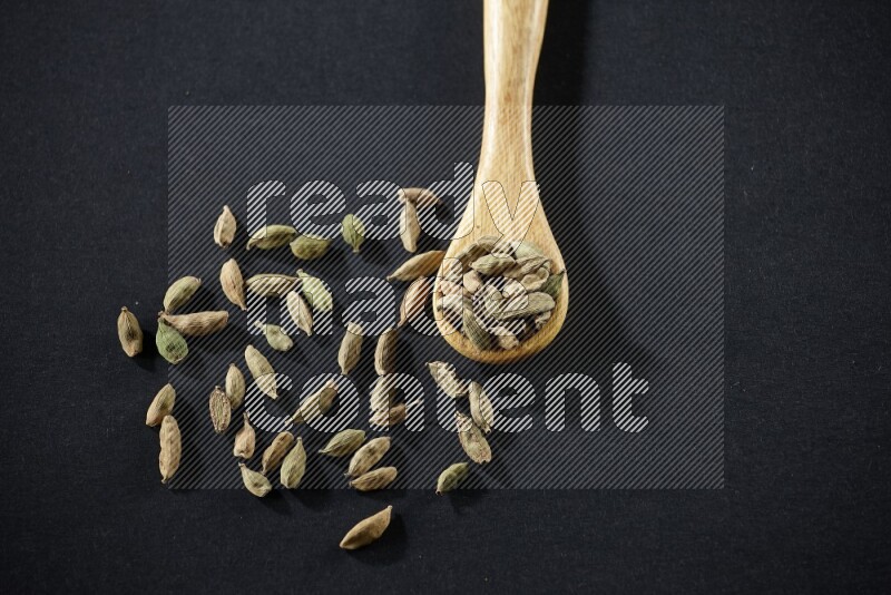 A wooden spoon full of cardamom on black flooring