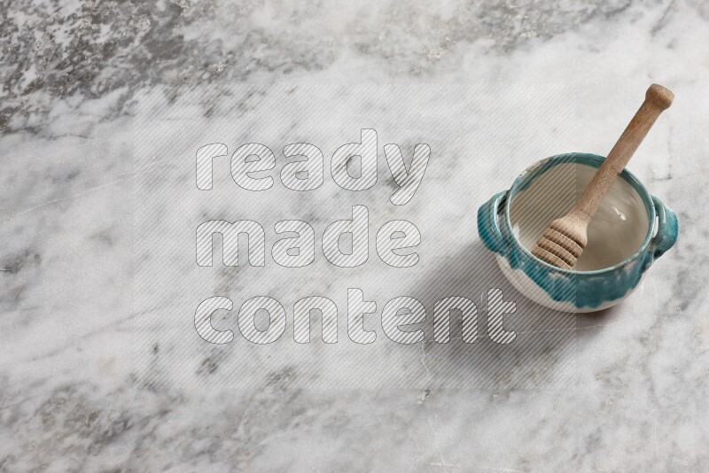 Multicolored pottery bowl with wooden honey dipper in it on grey marble background