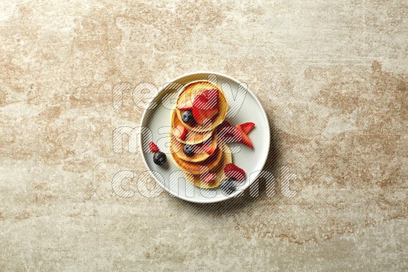Five stacked mixed berries mini pancakes in a blue plate on beige background